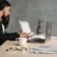Obraz przedstawia niewyraźnie zarysowaną postać kobiety siedzącej przy stole, zajmującej się pracą. Na pierwszym planie widać laptopa, filiżankę kawy, długopisy oraz dokumenty leżące na stole. Tło jest rozmyte, co skupia uwagę na przedmiotach na stole.