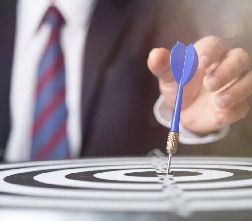 Społeczna odpowiedzialność biznesu a niepełnosprawność 3 Obrazek wyróżniający w artykule - społeczna odpowiedzialność biznesu. Na zdjęciu dłoń mężczyzny w garniturze, wbijająca lotkę w środek tarczy. Zdjęcie sugeruje osiągnięcie sukcesu w drodze odpowiedzialnego prowadzenia biznesu.