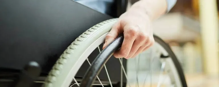 Na zdjęciu widać zbliżenie dłoni osoby poruszającej się na wózku inwalidzkim. Ręka pewnie chwyta obręcz koła, co symbolizuje samodzielność, siłę i codzienną determinację. To obraz cichej, ale wytrwałej walki o niezależność. Jasne, miękkie światło w tle dodaje scenie ciepła i nadziei. Ten obraz może towarzyszyć treściom odpowiadającym na pytanie jak zatrudnić osobę niepełnosprawną, bo oddaje nie tylko fizyczny aspekt niepełnosprawności, ale też doświadczenie, w którym ważne są szacunek, dostępność i równość szans.