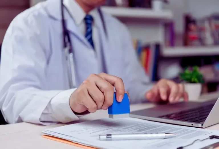 Lekarz w białym fartuchu stemplujący dokumenty na biurku – procedura orzecznicza i dokumentacja medyczna potwierdzająca schorzenia specjalne i szczególne PFRON
