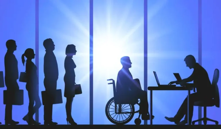 Na ilustracji widać sylwetki osób stojących w kolejce na rozmowę kwalifikacyjną, w tym osobę poruszającą się na wózku inwalidzkim. Siedzi ona naprzeciwko rekrutera przy biurku, z promiennym światłem słonecznym w tle, które symbolicznie rozjaśnia przestrzeń między nimi. Obrazek przedstawia równość szans i nadzieję na dostęp do zatrudnienia bez barier. Uświadamia znaczenie hasła przyjazne środowisko pracy dla osób z niepełnosprawnościami – miejsca, w którym każdy kandydat może liczyć na sprawiedliwe traktowanie, niezależnie od swojej sprawności.