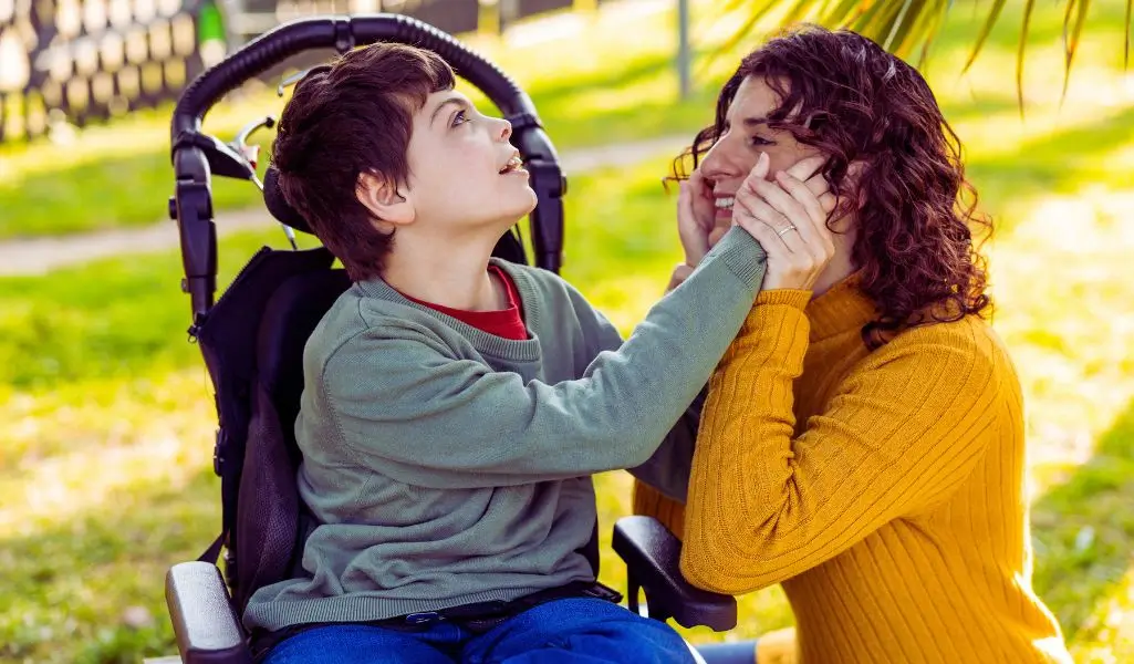 Świadczenie pielęgnacyjne 2025 dla opiekunów osób niepełnosprawnych od A do Z 3 Matka tuląca dziecko z niepełnosprawnością siedzące na wózku, wspólna chwila bliskości i opieki, którą umożliwia świadczenie pielęgnacyjne