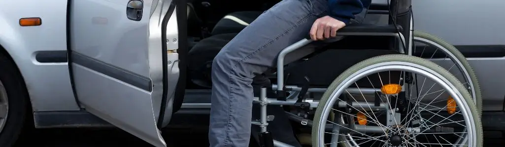 Obrazek wyróżniający do artykułu - samochód dla niepełnosprawnych. Widoczna osoba przesiadająca się z wózka na fotel kierowcy w aucie.