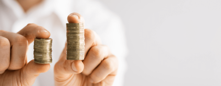 Na zdjęciu widoczne są dwie dłonie trzymające stosy monet – jeden niski, drugi znacznie wyższy. Kontrast między małą a dużą wieżą monet symbolizuje różnicę w wydatkach, pokazując w prosty sposób, jak mogą wyglądać koszty płacy PFRON. Obraz przywołuje skojarzenia z porównywaniem, kalkulacją i poszukiwaniem oszczędności. Może budzić odczucie napięcia między tym, co niewielkie i łatwe do udźwignięcia, a tym, co większe i trudniejsze do zbalansowania w codziennych decyzjach finansowych.