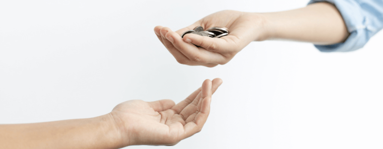 Zbliżenie dwóch dłoni na jasnym tle: górna dłoń przekazuje kilka monet, dolna czeka na wsparcie. Gest budzi skojarzenia z zaufaniem, odpowiedzialnością i realną pomocą finansową — nawiązanie do: ekwiwalent w kosztach płacy PFRON.