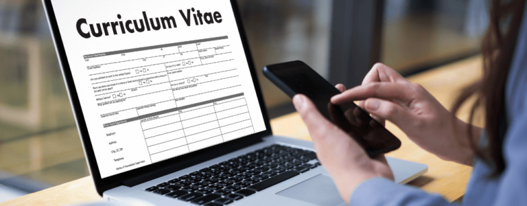 Osoba korzysta z telefonu przed laptopem z otwartym dokumentem „Curriculum Vitae” – ilustracja tematu umiejętności do CV.