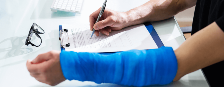 Osoba z niepełnosprawnością z ręką w opatrunku wypełnia dokument na biurku – list motywacyjny osoby niepełnosprawnej.