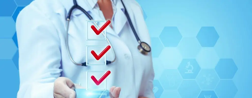 Jak działa lista chorób do bezterminowego orzeczenia o niepełnosprawności? 1 Obraz przedstawia postać osoby w białym kitlu, najprawdopodobniej lekarza. Postać jest sfotografowana od klatki piersiowej w górę. Na szyi widać stetoskop. Na pierwszym planie po lewej stronie znajduje się przezroczysty panel z trzema prostokątnymi polami, każde z czerwoną ikoną "ptaszka" oznaczającą listę chorób do orzeczenia. Tło jest niebieskie z sześciokątnymi wzorami i ikonami symbolizującymi różne aspekty medycyny, takie jak mikroskop, pigułki czy narzędzia medyczne.