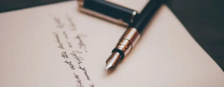 Obrazek wyróżniający do artykułu - mądre cytaty. Na obrazku znajduje się zbliżenie na wieczne pióro leżące na kartce papieru. Pióro jest czarno-srebrne, z odkrytą stalówką, gotowe do pisania. Na kartce widać ręcznie napisany tekst, choć szczegóły treści są nieczytelne z powodu rozmycia obrazu. Tło jest proste, co pozwala skupić uwagę na piórze i kartce.