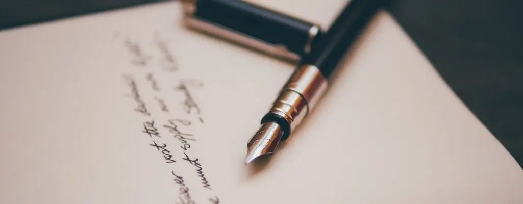 Obrazek wyróżniający do artykułu - mądre cytaty. Na obrazku znajduje się zbliżenie na wieczne pióro leżące na kartce papieru. Pióro jest czarno-srebrne, z odkrytą stalówką, gotowe do pisania. Na kartce widać ręcznie napisany tekst, choć szczegóły treści są nieczytelne z powodu rozmycia obrazu. Tło jest proste, co pozwala skupić uwagę na piórze i kartce.