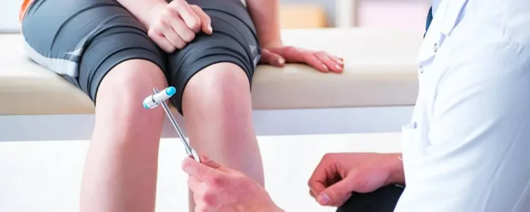 obrazek główny we wpisie o tytule "Rehabilitacja neurologiczna. Kompleksowy poradnik dla pacjentów i nie tylko" Na obrazku lekarz neurolog wykonujący badanie. Widać pacjenta siedzącego na łózku. Lekarz ostukuje widoczne kolana pacjenta