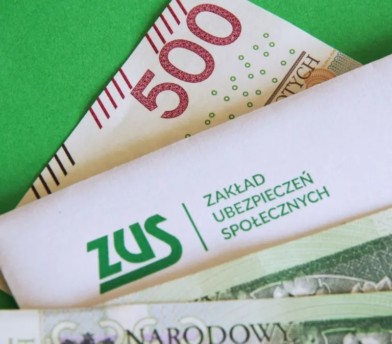 Obrazek wyróżniający do artykułu 500 plus dla niepełnosprawnych. Na zdjęciu koperta z logiem ZUS, a pod nią stosik banknotów 500 złotowych.