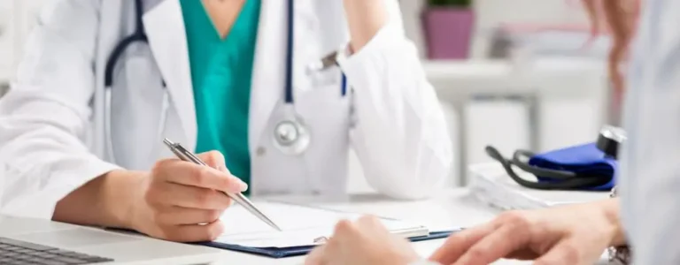 Lekarz w białym fartuchu omawia dokumenty z pacjentem w gabinecie, co oddaje atmosferę rozmowy o zdrowiu i formalnościach, np. jak uzyskać orzeczenie o niepełnosprawności.