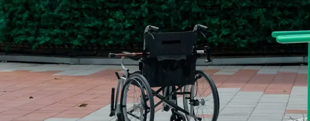 Zdjęcie w artykule - nabycie prawa do urlopu dodatkowego. Na zdjęciu pusty wózek inwalidzki stojący na chodniku. Scenka sugeruje nieobecność osoby niepełnosprawnej.