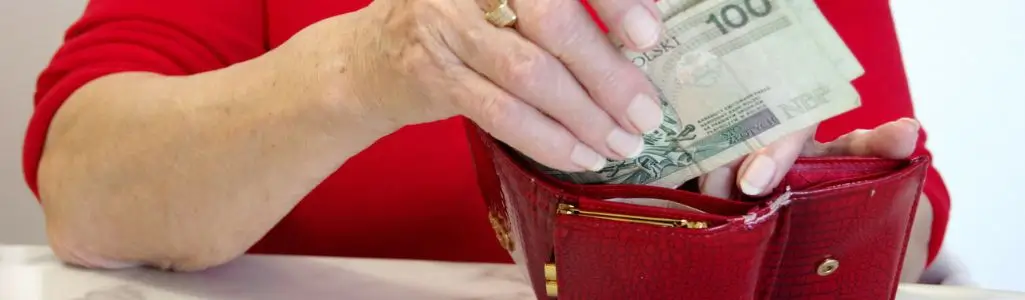 Obrazek wyróżniający do artykułu - ile wynosi dodatek pielęgnacyjny. Widoczna dłoń kobiety układającej banknoty do portfela.