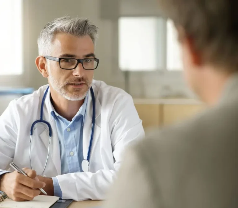 Obrazek wyróżniający do artykułu - ZUS wykaz chorób do renty. Na obrazku jest przedstawiony lekarz. Ma on na sobie białe lekarskie ubranie z niebieskim kołnierzykiem, a na szyi zawieszony stetoskop. Wygląda na skupionego i profesjonalnego, przeprowadza prawdopodobnie rozmowę z pacjentem. Zdjęcie może symbolizować proces ubiegania się o rentę ze względu na chorobę, gdzie ZUS jest instytucją odpowiedzialną za przyznanie świadczeń, a lekarz jest częścią procesu weryfikacji stanu zdrowia wnioskodawcy.