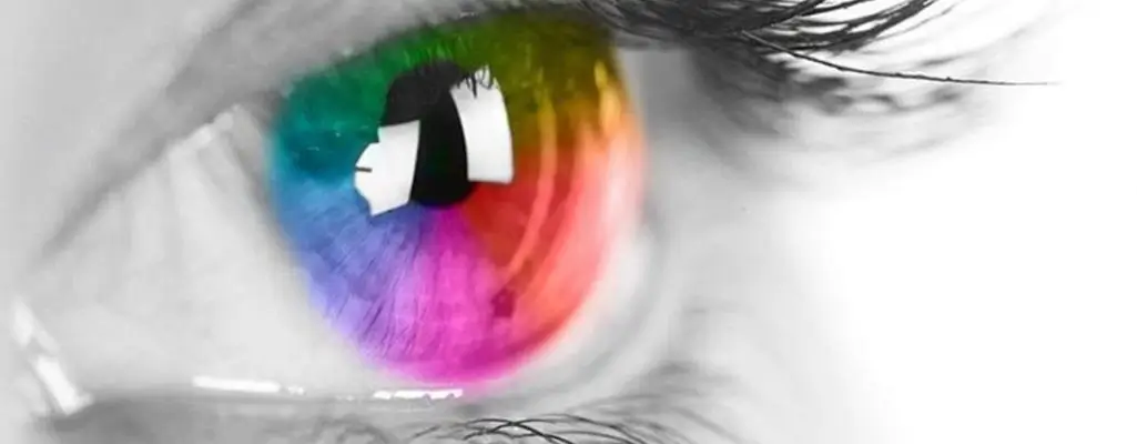 Zdjęcie w artykule - jak widzą daltoniści. Widoczny zbliżenie na oko z tęczówką żywo zabarwioną spektrum barw, co ilustruje koncepcję widzenia kolorów. Jednak reszta oka i tło są w skali szarości, co może sugerować, że zaburzenia widzenia kolorów mogą prowadzić do ograniczonego postrzegania kolorów w otaczającym, kolorowym świecie. Zdjęcie może być pouczające dla zrozumienia wpływu zaburzeń widzenia kolorów na codzienne życie.