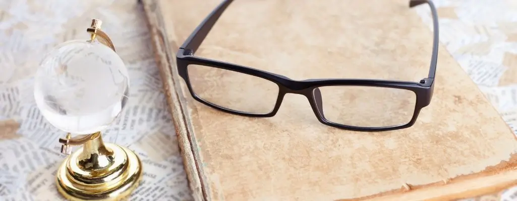 Zdjęcie w artykule - okulary do czytania Na obrazku znajduje się para czarnych okularów do czytania, które leżą na otwartej książce. Obok okularów umieszczony jest mały, okrągły szklany globus, który sugeruje że okularów do czytania potrzebują ludzie na całym świecie.