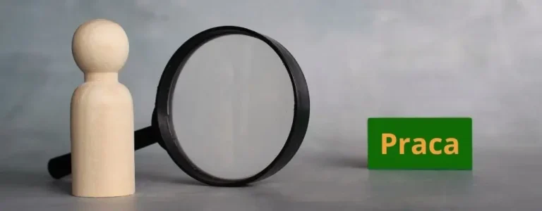 Obrazek wyróżniający do artykułu - jak szukać pracy. Widoczne zdjęcie przedstawia symboliczne narzędzie do poszukiwania pracy. Na zdjęciu znajduje się drewniana figurka człowieka w kształcie pionka, stojąca obok dużej lupki, przez którą jest ona przybliżana, co sugeruje "szukanie" lub "badanie" czegoś dokładniej. Na prawo od figurki i lupki umieszczono zielony prostokątny znak z napisem „Praca”, który w kontekście kompozycji podkreśla temat poszukiwania zatrudnienia. Tło jest neutralne i jednolite, co pozwala skupić uwagę na przedmiotach.