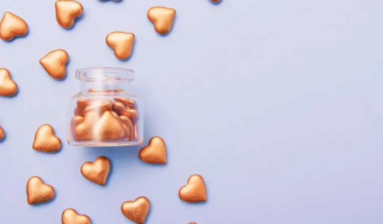 Obrazek wyróżniający do artykułu - jak zgłosić zbiórkę publiczną. Obrazek przedstawia słoik z przezroczystego szkła wypełniony małymi sercami w kolorze złotym. Słoik znajduje się na jasnoniebieskim tle, które zajmuje większość kadru. Dookoła słoika, na powierzchni tła, rozrzucone są złote serca, tworząc dekoracyjny wzór. Obrazek ma estetyczny, minimalistyczny charakter i może symbolizować miłość, troskę lub hojność.