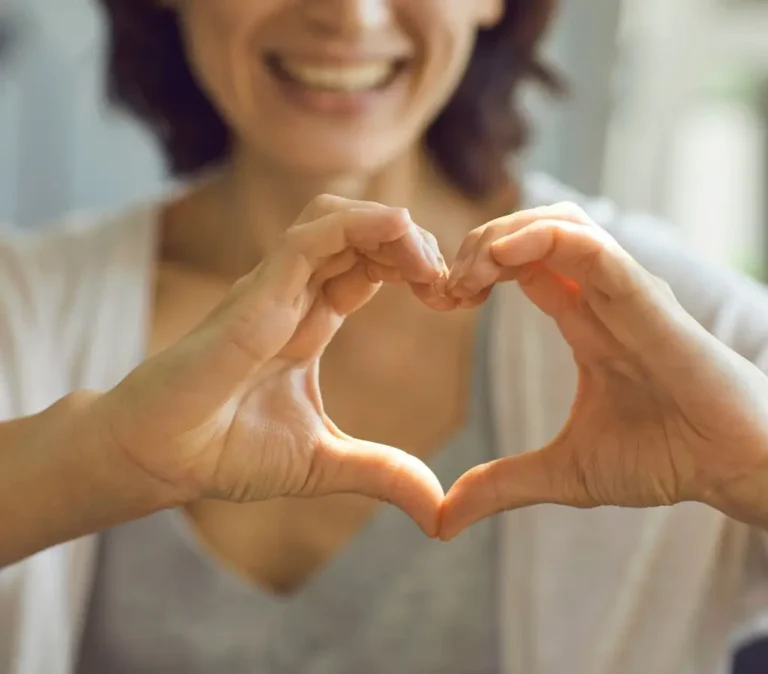 Obrazek wyróżniający do artykułu - na jaki cel można założyć zbiórkę publiczną. Obraz przedstawia osobę, która formuje dłońmi kształt serca. Osoba jest uśmiechnięta, co nadaje zdjęciu ciepłego i serdecznego charakteru. Całość kompozycji jest ciepła i przyjazna, co może sugerować tematykę związaną z miłością, serdecznością, wsparciem lub dobroczynnością. Obraz emanuje pozytywnymi emocjami i zachęca do myślenia o życzliwości i wsparciu dla innych.