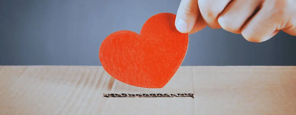 Poznaj zasady, na jakich działają zbiórki publiczne, byś działał zgodnie z prawem 3 Obrazek wyróżniający do artykułu - zbiórki publiczne. Obrazek przedstawia rękę wkładającą czerwone, drewniane serce do szczeliny w kartonowym pudełku. Pudełko jest koloru brązowego, a tło obrazka jest w odcieniach szarości, co sprawia, że czerwone serce jest centralnym punktem obrazu. Obrazek może symbolizować akt dobroczynności, miłości lub wsparcia, gdzie serce reprezentuje coś cennego i osobistego, wkładanego do pudełka, które może symbolizować darowiznę lub zbiórkę publiczną.