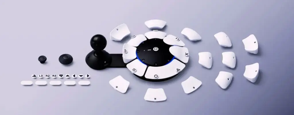 Zdjęcie do artykułu - playstation access kontroler dla niepełnosprawnych. Zdjęcie przedstawia specjalistyczny kontroler, zaprojektowany prawdopodobnie do ułatwienia rozgrywki osobom z niepełnosprawnościami. Kontroler ma okrągły kształt i jest wyposażony w czarne centralne pokrętło otoczone przez białe segmenty, które pełnią rolę przycisków. Każdy z segmentów ma unikalny kształt i symbol, co wskazuje na ich przypisane funkcje. Po lewej stronie znajdują się różne wymienne elementy, w tym kulisty joystick i inne kształty, które mogą być zamieniane na kontrolerze. Układ przycisków sugeruje, że jest to urządzenie modułowe, zaprojektowane z myślą o personalizacji, aby dostosować kontroler do indywidualnych potrzeb użytkownika. Kolorystyka jest stonowana, z przewagą bieli i czerni, co nadaje mu nowoczesny wygląd.