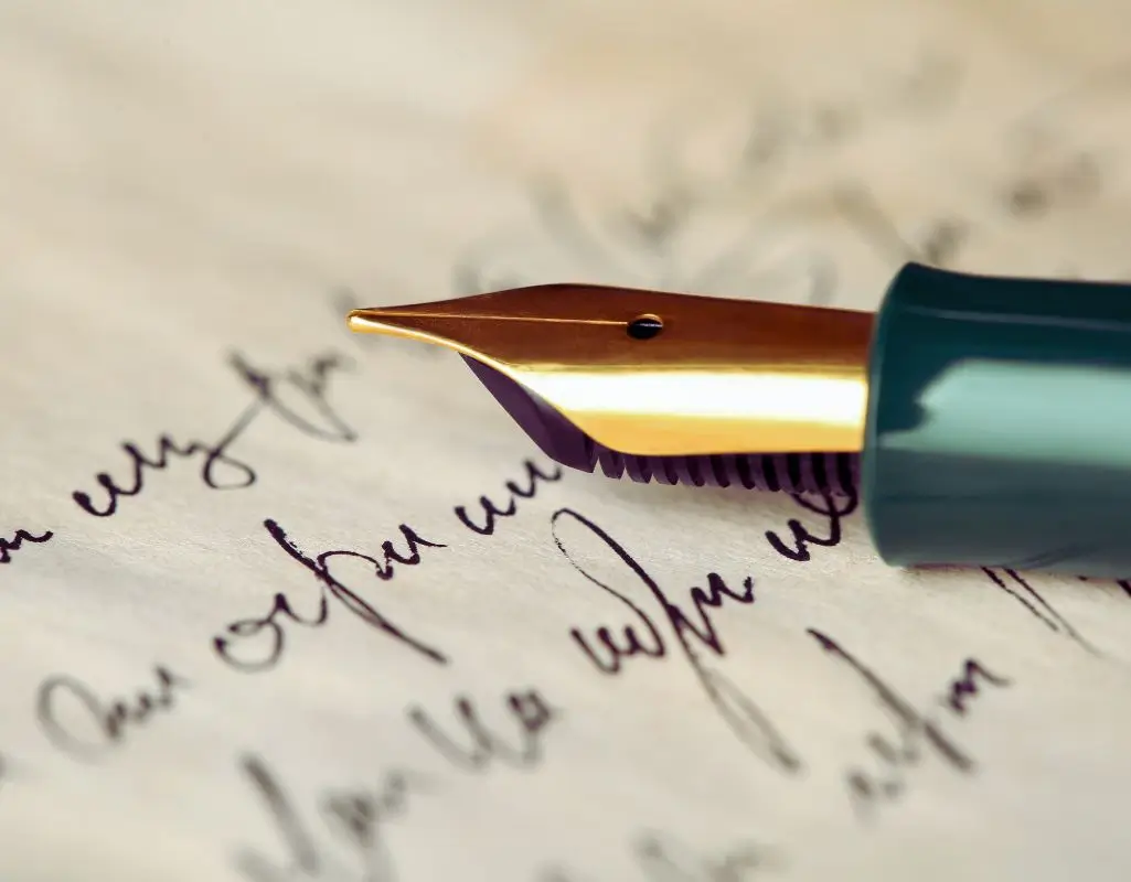 Obrazek do artykułu - cytaty o niepełnosprawności. Na obrazie widać zbliżenie na pióro wieczne z metalową, złoto-srebrną stalówką, która znajduje się nad arkuszem papieru. Na papierze widnieje odręczne pismo napisane atramentem, w kolorze ciemnym, prawdopodobnie czarnym lub granatowym. Pismo jest nieco pochyłe, z charakterystycznymi zakrzywieniami liter, co sugeruje płynny i elegancki styl pisania. Obraz jest skoncentrowany na stalówce pióra i fragmencie tekstu, tworząc wrażenie artystyczne i nostalgiczne, związane z tradycyjną formą pisania.