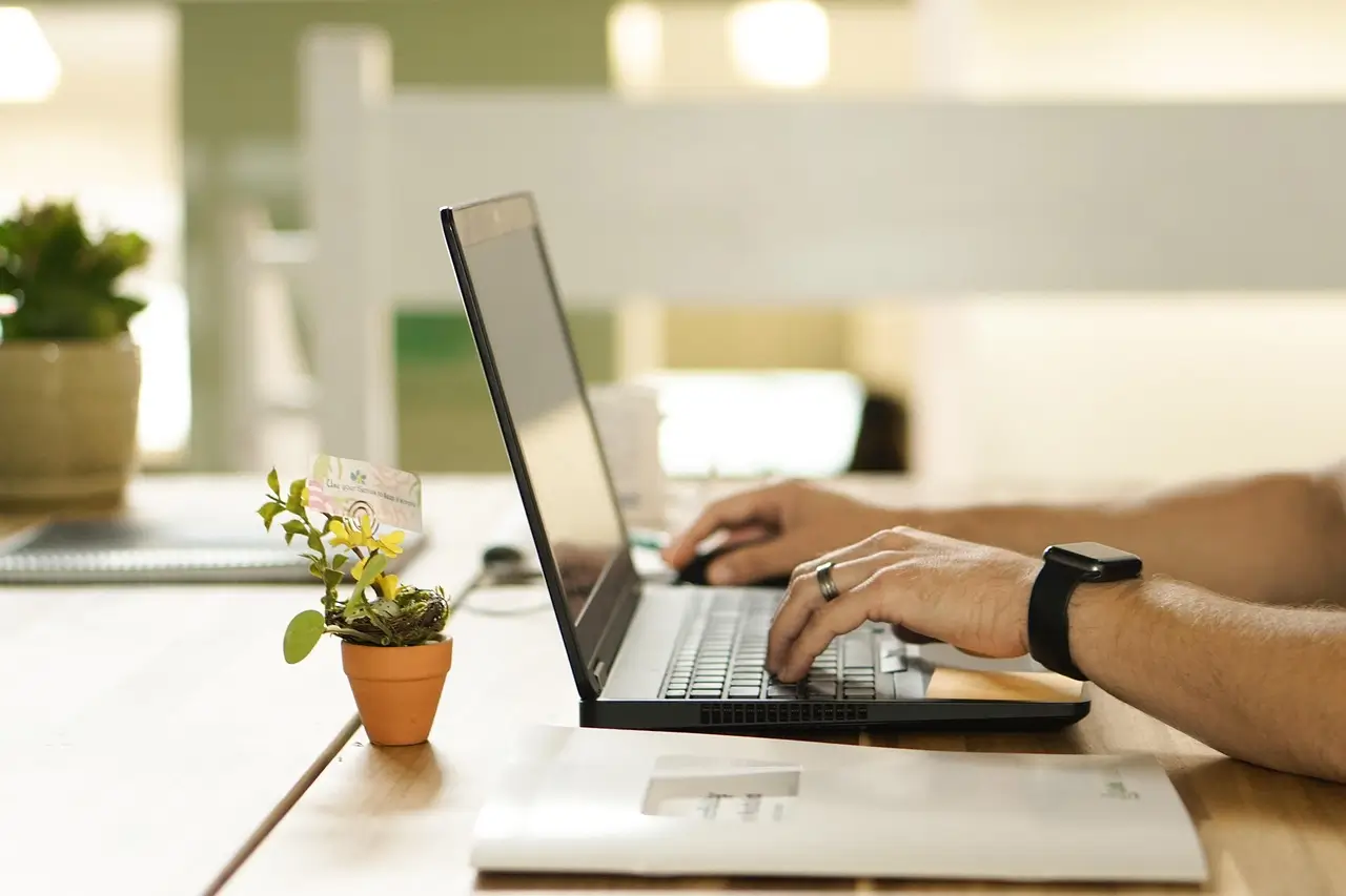 Jak psycholog online otwiera drzwi do emocjonalnego wsparcia 1 Osoba korzystająca z laptopie w domowym biurze, z małą rośliną w doniczce na biurku, w jasnym i spokojnym otoczeniu.