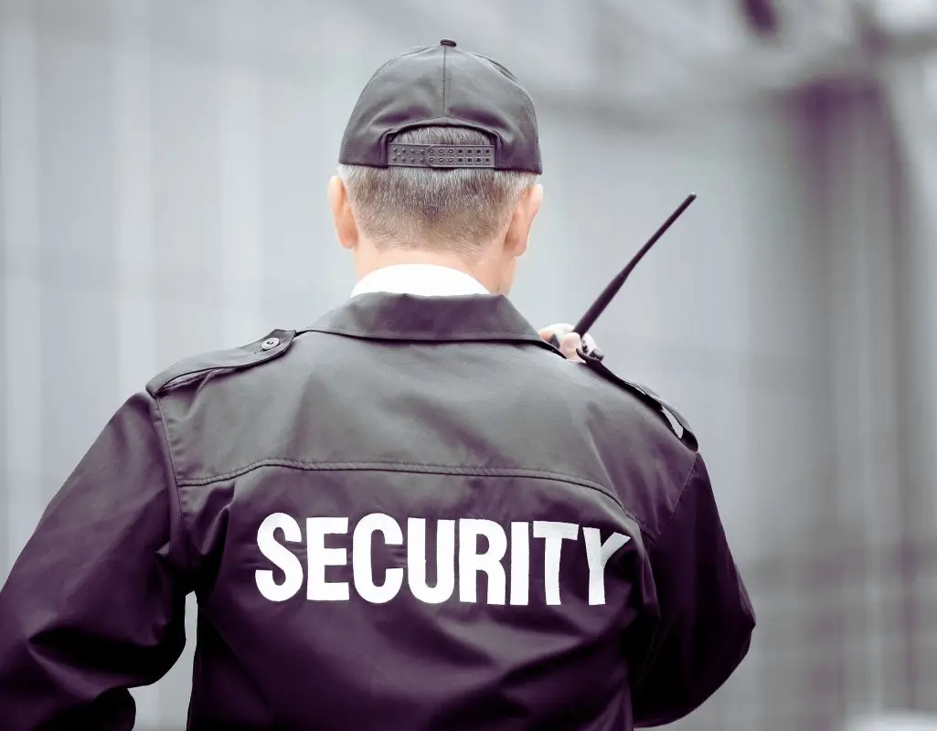 Jak zostać kwalifikowanym pracownikiem ochrony. Ochroniarz w kurtce z napisem 'SECURITY', trzymający krótkofalówkę.