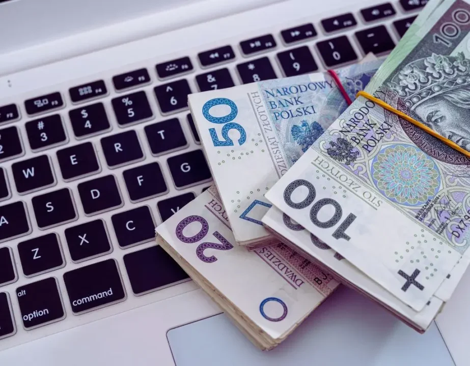 Jak zmieniło się dofinansowanie wynagrodzeń PFRON od stycznia 2025? Stawki, wyrównanie 4 Obrazek do artykułu dofinansowanie wynagrodzeń PFRON w 2025. Na zdjęciu widać polskie banknoty w nominałach 20, 50 i 100 złotych, ułożone w stosy na klawiaturze laptopa. Ostre, wyraziste kolory pieniędzy kontrastują z czarnymi klawiszami, co może wzbudzać skojarzenia z przepływem gotówki i możliwościami finansowymi.