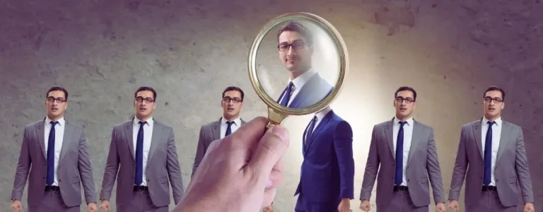 Na obrazie widzimy grupę mężczyzn ubranych w eleganckie garnitury, ustawionych w rzędzie. W centrum uwagi znajduje się jeden z nich, wyróżniony przez szkło powiększające trzymane w dłoni. Dzięki szkłu powiększającemu jego postać wydaje się jaśniejsza, bardziej wyrazista i profesjonalna. Tło obrazu jest subtelne i neutralne, co pozwala skupić się na symbolice wyboru idealnego kandydata. Obraz wywołuje uczucie dokładności, selekcji i profesjonalizmu, podkreślając korzyści z usług agencji pracy, takich jak wsparcie w znalezieniu odpowiedniego kandydata czy pomoc w dopasowaniu do konkretnego stanowiska.