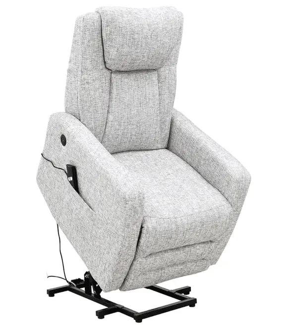 Na zdjęciu znajduje się nowoczesny, elektryczny fotel wypoczynkowy z funkcją podnoszenia. Tapicerka fotela ma jasnoszary kolor z delikatnym, melanżowym wzorem przypominającym strukturę lnu lub grubo tkanego materiału. Fotel wyposażony jest w wysokie, dobrze wyprofilowane oparcie z dodatkowym zagłówkiem oraz szerokie podłokietniki. Znajduje się w pozycji częściowo uniesionej – jego siedzisko jest lekko podniesione i pochylone ku przodowi, co ułatwia wstawanie. Na bocznej części fotela znajduje się wszyta kieszeń, w której widoczny jest przewodowy pilot z przyciskami sterującymi, służący do regulacji pozycji oparcia, siedziska i funkcji podnoszenia. Fotel opiera się na czarnej metalowej ramie z prostokątną podstawą – mechanizm ten umożliwia unoszenie całej konstrukcji. Styl mebla łączy w sobie funkcjonalność i estetykę, a całość zaprojektowana jest z myślą o osobach starszych lub z ograniczoną mobilnością.