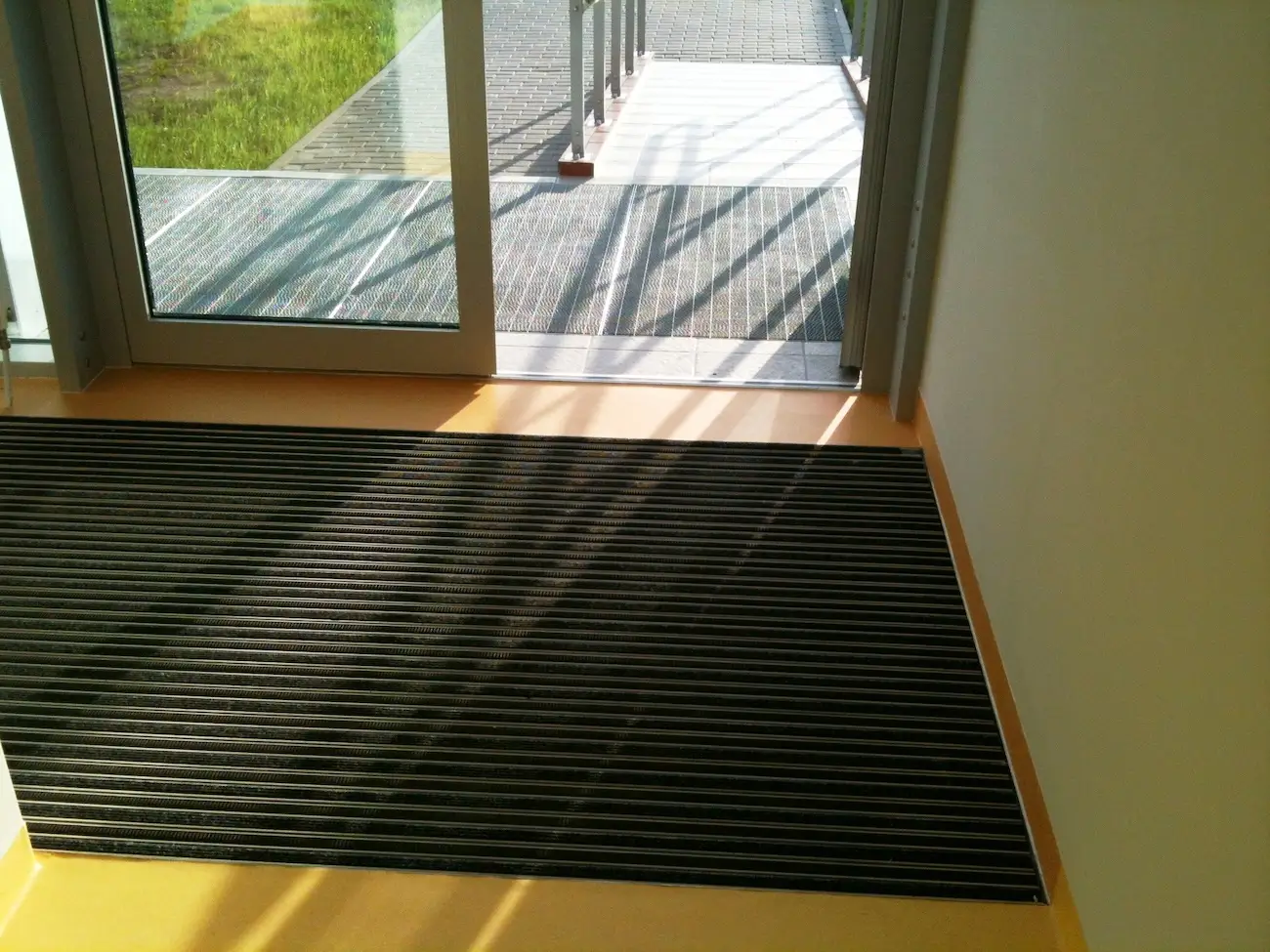 Jak zaprojektować bezpieczne wejście do budynku dla osób z niepełnosprawnościami? 1 Wejście do budynku z szerokimi drzwiami i zamontowanymi wycieraczkami systemowymi wewnątrz i na zewnątrz – rozwiązanie zapewniające bezpieczeństwo, komfort oraz dostępność dla wszystkich użytkowników, w tym osób z niepełnosprawnościami i rodzin z dziećmi.