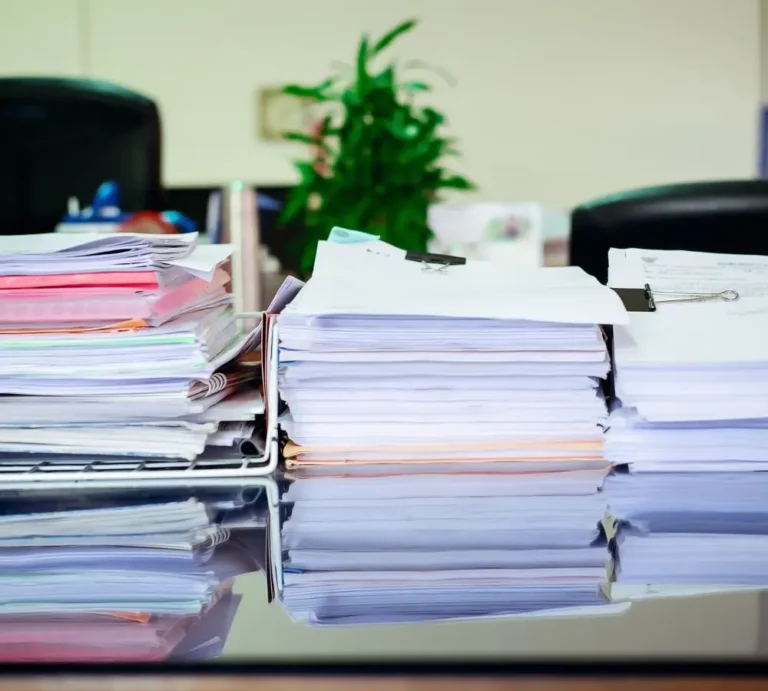 Stosy uporządkowanych dokumentów spiętych klipsami i posegregowanych w plastikowych tackach na biurku w biurze – symbol potrzeby dobrej organizacji pracy z użyciem akcesoriów biurowych.