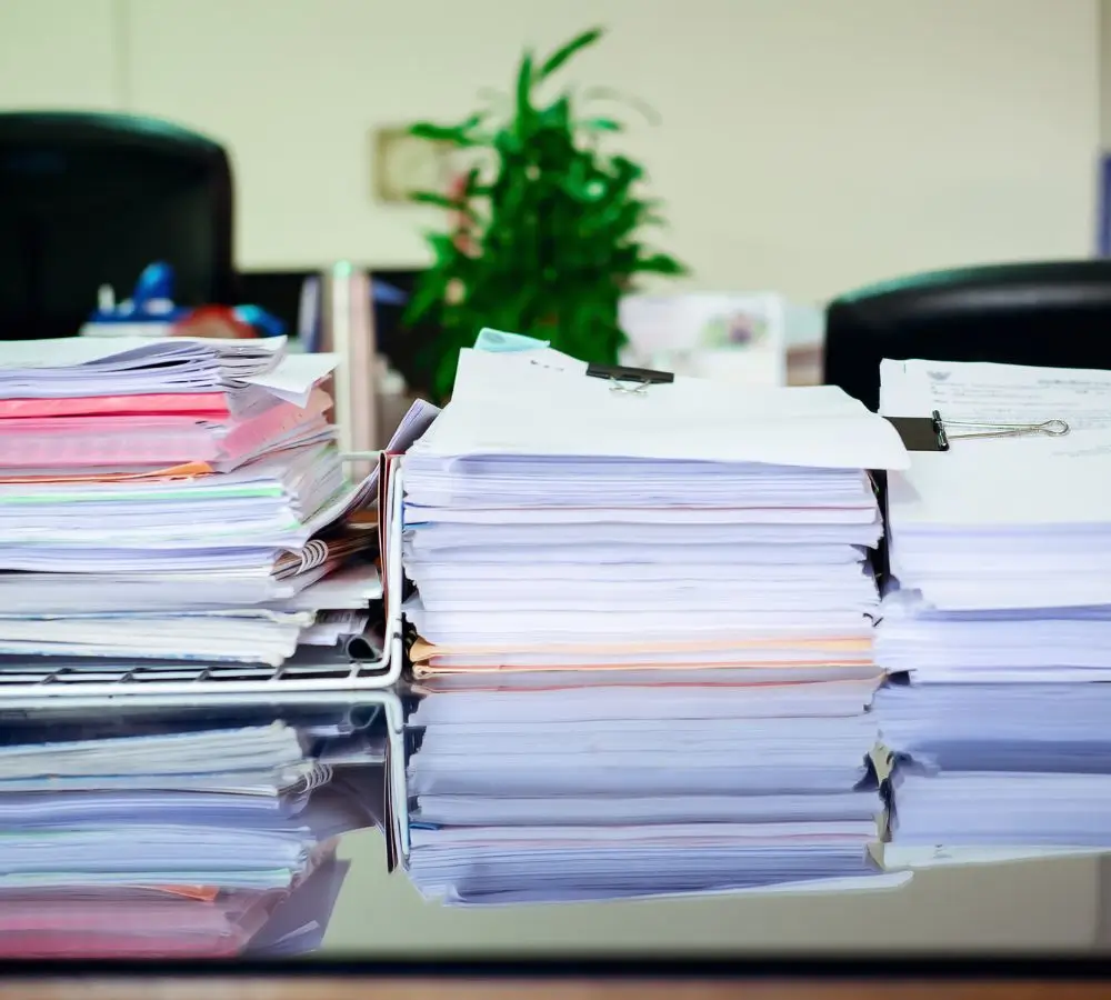 Jak gilotyna i bindownica mogą usprawnić pracę Twojego biura 1 Stosy uporządkowanych dokumentów spiętych klipsami i posegregowanych w plastikowych tackach na biurku w biurze – symbol potrzeby dobrej organizacji pracy z użyciem akcesoriów biurowych.