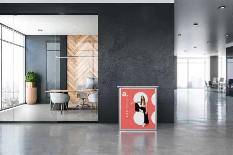 Nowoczesne wnętrze biurowe z trybunką reklamową ustawioną przy ciemnej ścianie – na trybunce widoczna kolorowa grafika z logotypem i zdjęciem kobiety w dynamicznej pozie, co pokazuje, jak dobrze zaprojektowana trybunka może przyciągać uwagę i wyróżniać markę podczas eventów i targów.