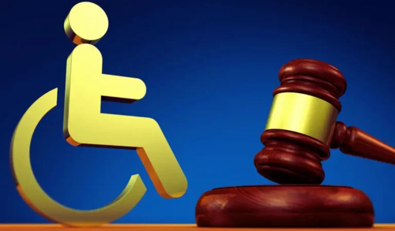 Na ilustracji widać złoty symbol osoby na wózku inwalidzkim, umieszczony obok sędziowskiego młotka, który leży na podstawce. Tło jest ciemnoniebieskie, co podkreśla powagę tematu. Obraz wywołuje skojarzenia z walką o prawa, sprawiedliwość i równość osób z niepełnosprawnością. Sugeruje potrzebę ochrony ich praw, zwłaszcza w kontekście tak trudnego zjawiska jak dyskryminacja osób niepełnosprawnych w pracy. To wizualne przypomnienie, że każda osoba zasługuje na sprawiedliwe traktowanie i równy dostęp do zatrudnienia.