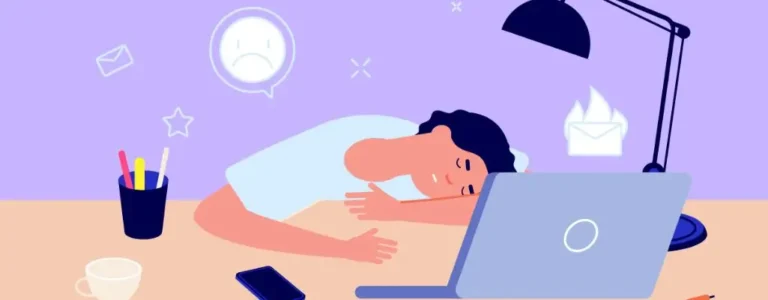 Ilustracja przedstawia osobę przy biurku, opartą głową o blat w geście bezsilności i zmęczenia. Na biurku znajduje się laptop, telefon, filiżanka i kubek z długopisami, a całość oświetla lampka biurkowa. W tle widać symbole przeciążenia – smutną buźkę, płonące wiadomości i nieprzeczytane maile, co podkreśla uczucie przytłoczenia obowiązkami. Obrazek oddaje emocjonalny stan osoby zmagającej się z brakiem energii i motywacji – to wizualna metafora momentu, w którym pojawia się pytanie, jak radzić sobie z wypaleniem zawodowym.