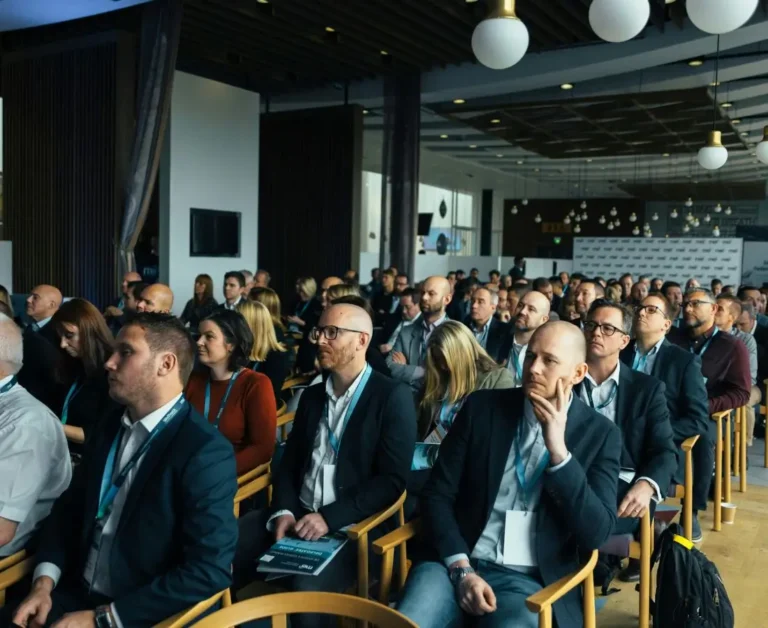 Pełna sala uczestników konferencji biznesowej – dziesiątki kobiet i mężczyzn w garniturach i identyfikatorach słucha prelegenta z uwagą, co ilustruje zaangażowanie środowiska pracodawców w tematy związane z rynkiem pracy i możliwą integracją osób z niepełnosprawnościami.