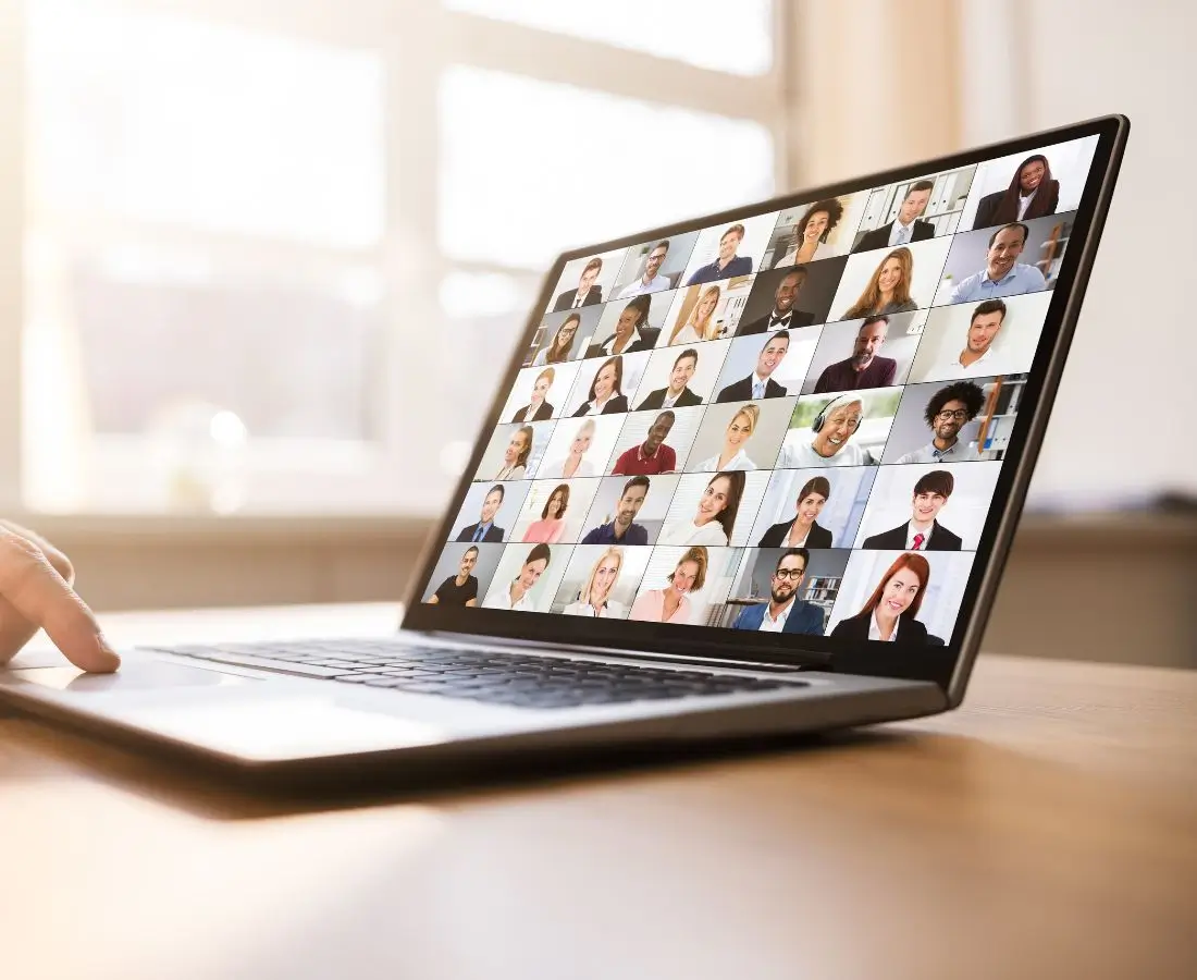 Jak zarabiać na swojej wiedzy, przy małej liczbie obserwujących w mediach społecznościowych 1 Laptop na biurku z wyświetlonym ekranem spotkania online, pokazującym kilkadziesiąt twarzy uczestników w trybie wideokonferencji. Obraz symbolizuje prowadzenie webinarów i szkoleń online – nawet dla kameralnej, ale zaangażowanej grupy odbiorców.