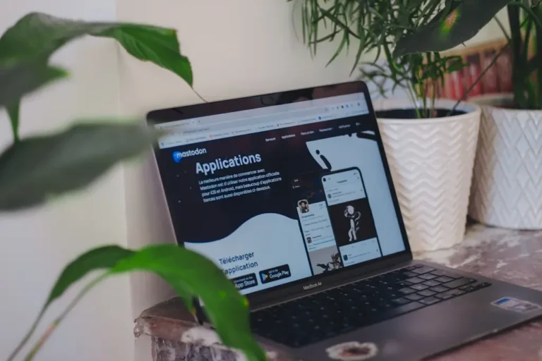 Jak przeprowadzić audyt dostępności strony internetowej? 2 Laptop z otwartą stroną aplikacji Mastodon, ustawiony na biurku obok roślin doniczkowych; ekran pokazuje elementy interfejsu mobilnego i tekst w języku francuskim – symbolizując konieczność sprawdzania dostępności treści cyfrowych także pod kątem języka, kontrastu, struktury oraz responsywności.