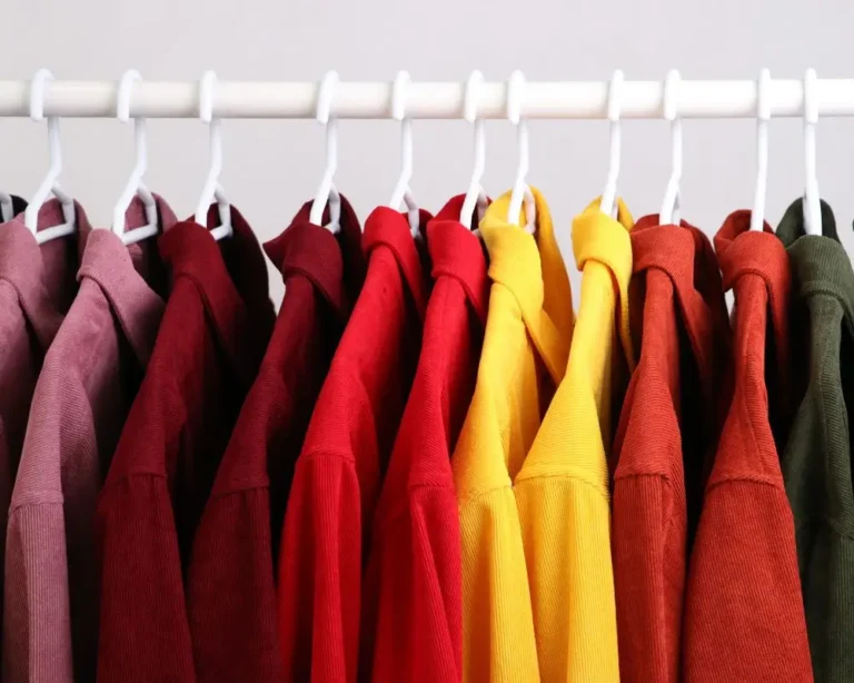 Szereg koszul wiszących na białym wieszaku, ułożonych według kolorów w ciepłej tonacji – od różowego i bordowego przez czerwony, pomarańczowy, żółty, aż po oliwkowozielony. Przykład harmonijnego zestawienia barw, które może wzmacniać przekaz wizualny i przyciągać uwagę w kampaniach reklamowych.