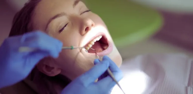 Kiedy NFZ refunduje leczenie zębów w narkozie dla niepełnosprawnych? 7 Dorosła pacjentka z zamkniętymi oczami leży na fotelu stomatologicznym, a dentysta w niebieskich rękawiczkach delikatnie bada jej zęby w jasnym świetle lampy; atmosfera spokoju i ulgi jak w sytuacjach, kiedy NFZ refunduje leczenie zębów w narkozie dla niepełnosprawnych.