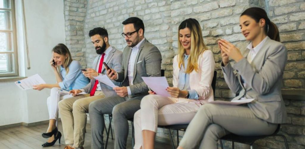 Kandydaci czekający na rozmowę kwalifikacyjną w eleganckich, biznesowych stylizacjach – przykład, jak się ubrać na rozmowę kwalifikacyjną, by zrobić dobre wrażenie.