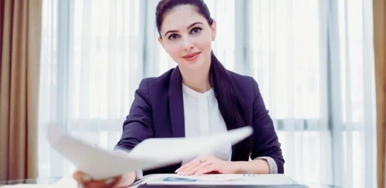 Kobieta w eleganckim stroju biurowym podaje dokument, symbolicznie pokazując, jak napisać podanie o pracę.